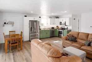 A modern kitchen with green cabinets, stainless steel appliances, and a dining area with a wooden table and chairs.