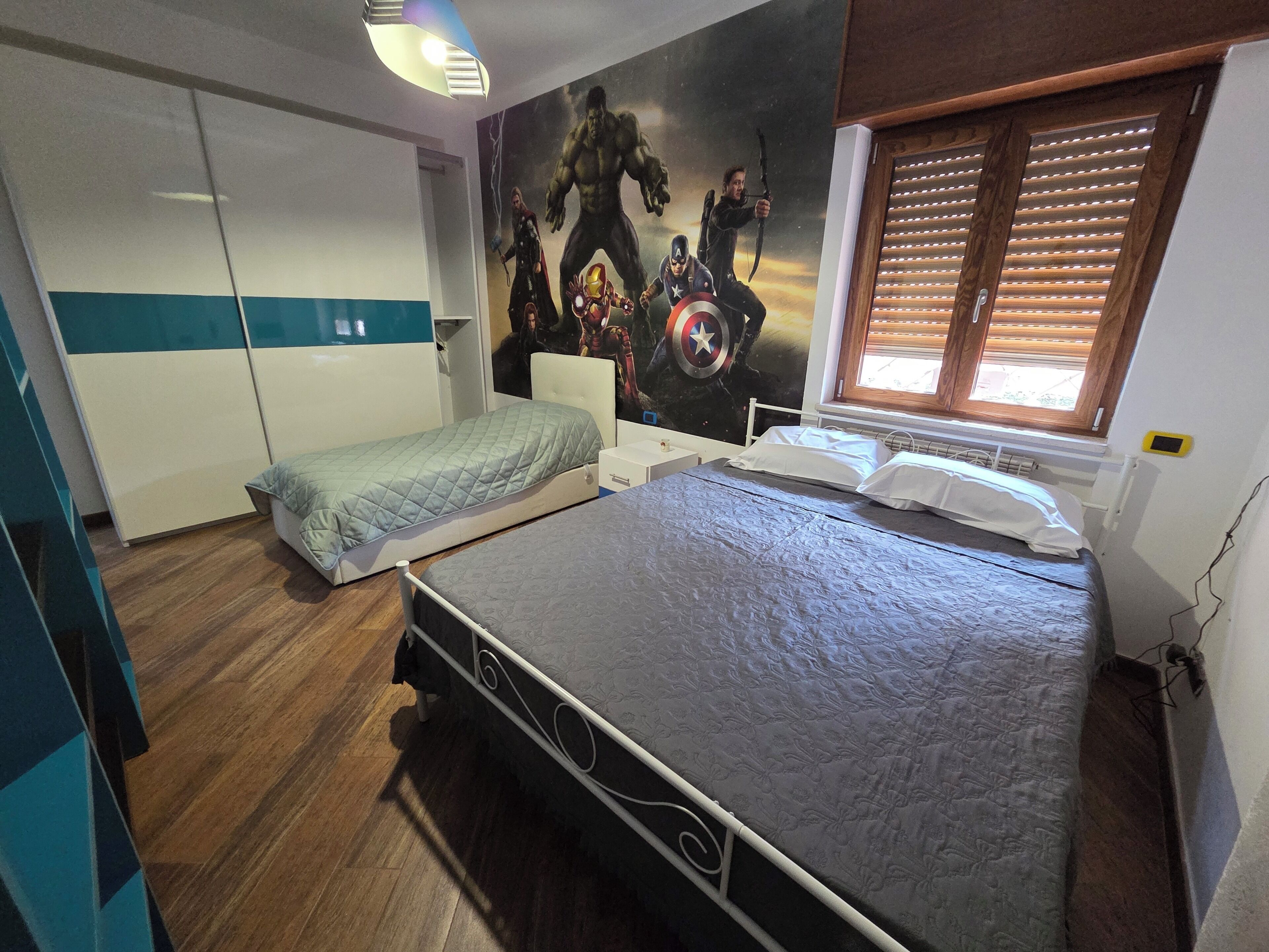 A bedroom with a bed, a wardrobe, and a mural on the wall.