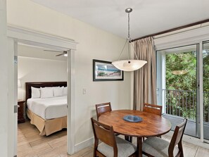 A hotel room with a bed, a dining table with chairs, a pendant light, and a large window with a view of greenery. - One Bedroom Condo in Lasata (Miramar Beach)