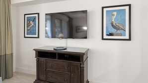Ein Zimmer mit einem wandmontierten Flachbildfernseher, einem dunklen Holzschrank darunter und zwei gerahmten Bildern an jeder Seite des Fernsehers.