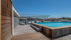 Uma área de piscina com deck de madeira, espreguiçadeiras e um pérgola.