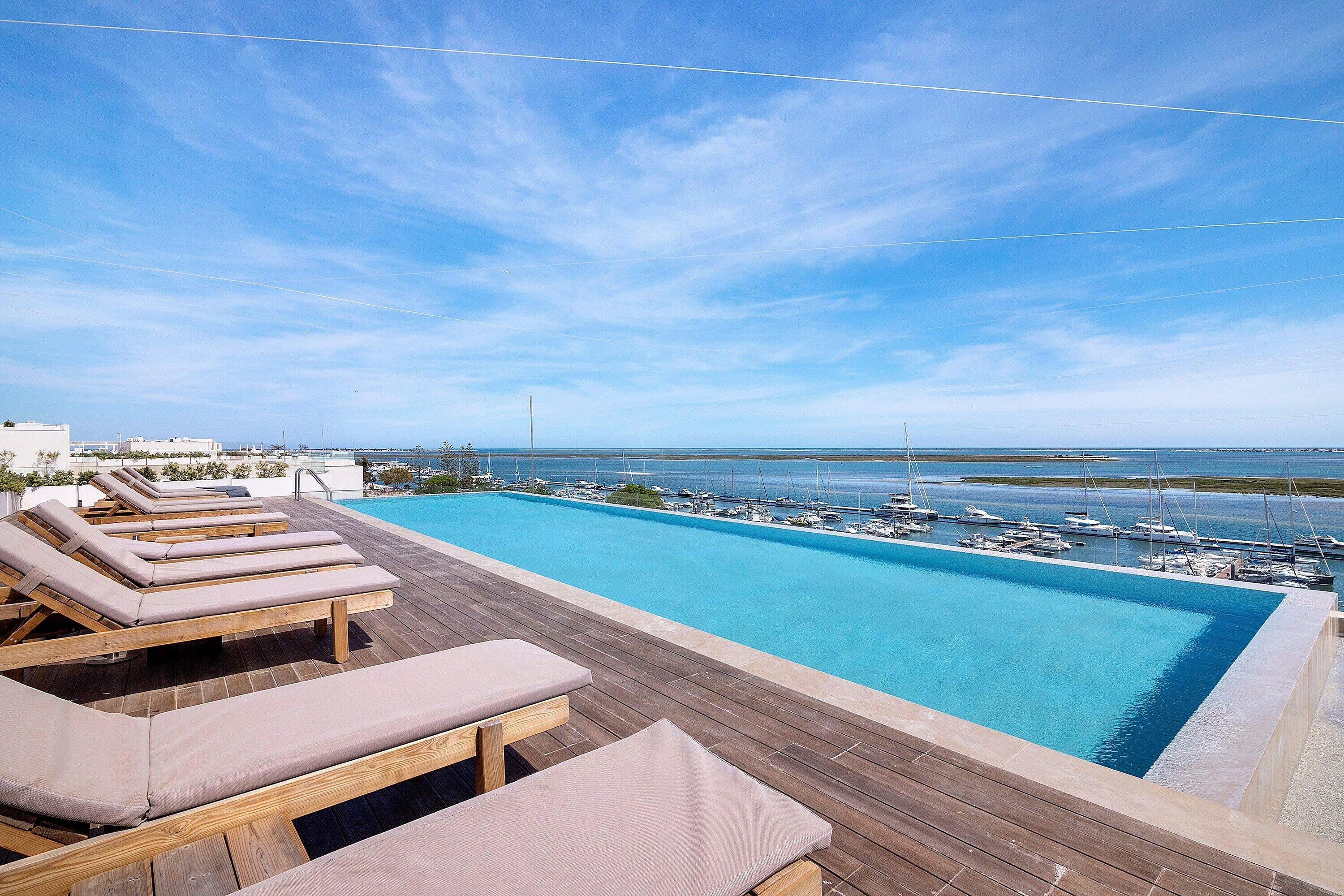 Ein Pool auf dem Dach mit Liegestühlen, einer Holzterrasse und Blick auf eine Marina.