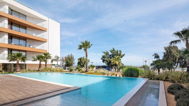A modern hotel with a swimming pool, wooden deck, and palm trees. - Ria Front Paradise – A Gem Facing the Ria (Olhão)