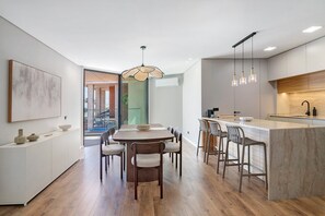 Een moderne keuken met een centraal eiland, barstoelen en een eettafel met stoelen.