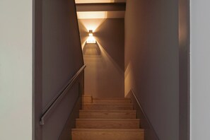 Eine Holztreppe mit Handlauf, die zu einer Lichtquelle führt.