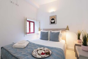 Ein ordentlich bezogenes Bett mit einer blauen und weißen Bettdecke, einem Tablett mit einer Tasse und einer Schale mit Obst auf dem Bett.