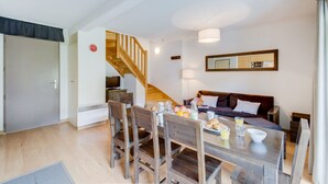 Ein modernes Wohnzimmer mit einer Holztreppe, einem Esstisch mit Stühlen, einer Couch und einer Küchenzeile inklusive Mikrowelle.