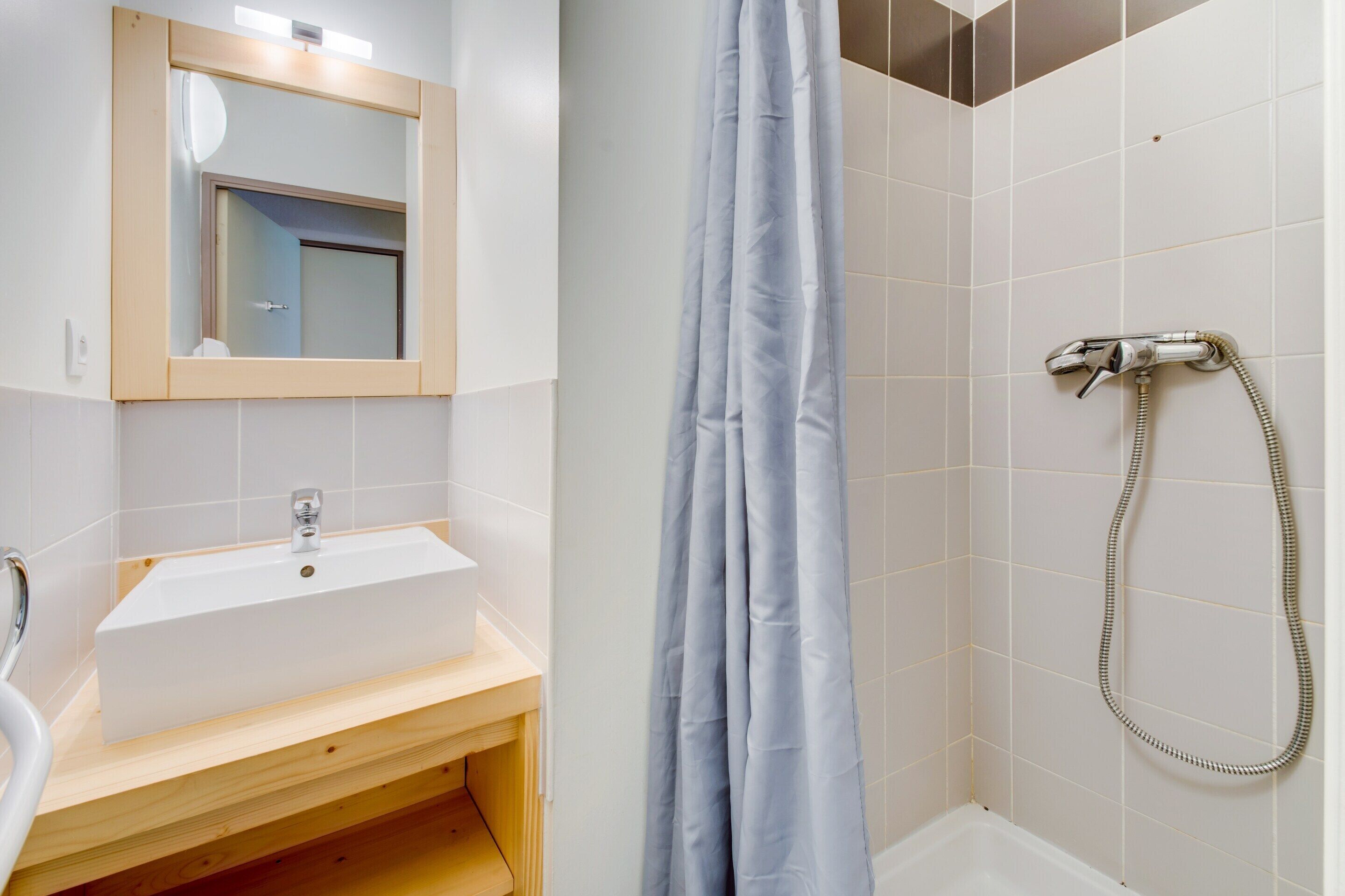 Un bagno con lavandino, specchio, doccia e tenda.