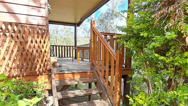 A wooden staircase leading to a covered porch with a view of trees and a garden.