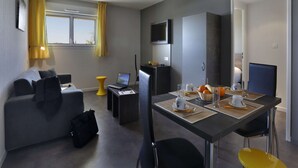 A modern living room with a sofa, a dining table set for two, a laptop, and a television on the wall. - Montpellier Base Near Coast With Balcony (Saint-Jean-de-Vedas)