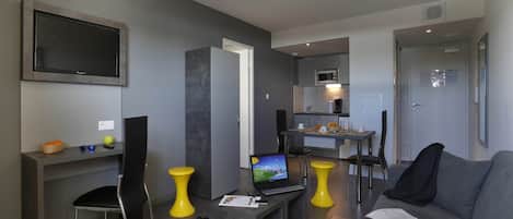 Una sala de estar moderna con un televisor de pantalla plana, un comedor con mesa y sillas, un sofá y una pequeña cocina con microondas.