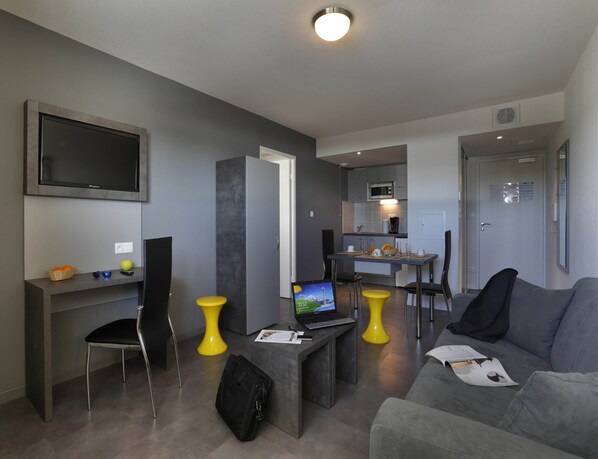 A modern living room with a flat-screen TV, a dining area with a table and chairs, a sofa, and a small kitchen area with a microwave. - Montpellier Base Near Coast With Balcony (Saint-Jean-de-Vedas)