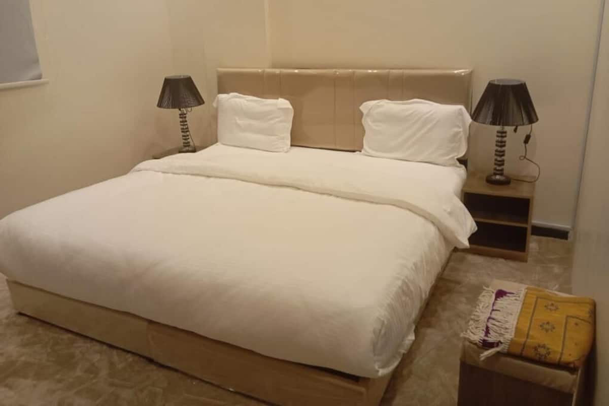 A bedroom with a large bed, two bedside lamps, a nightstand, and a small table with a lamp.