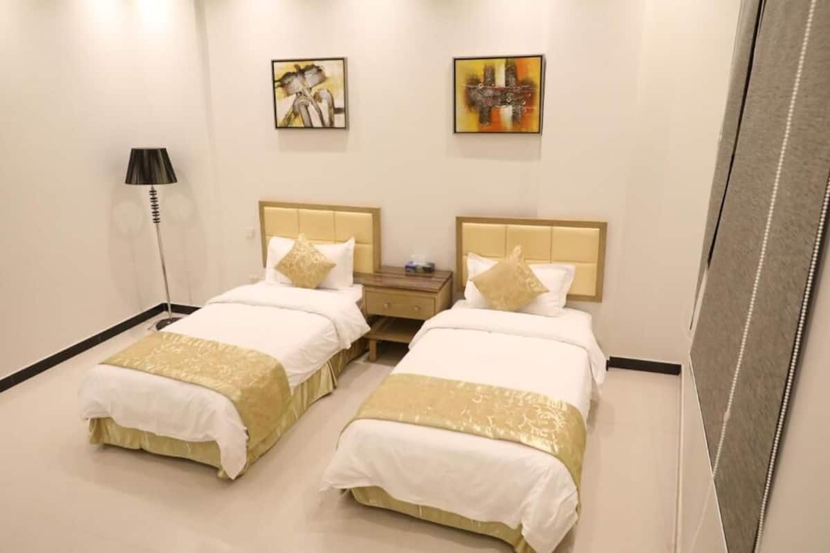 A hotel room with two beds, a nightstand, a lamp, and two paintings on the wall.