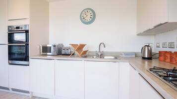 A modern kitchen with built-in appliances, a sink, and a wall clock.