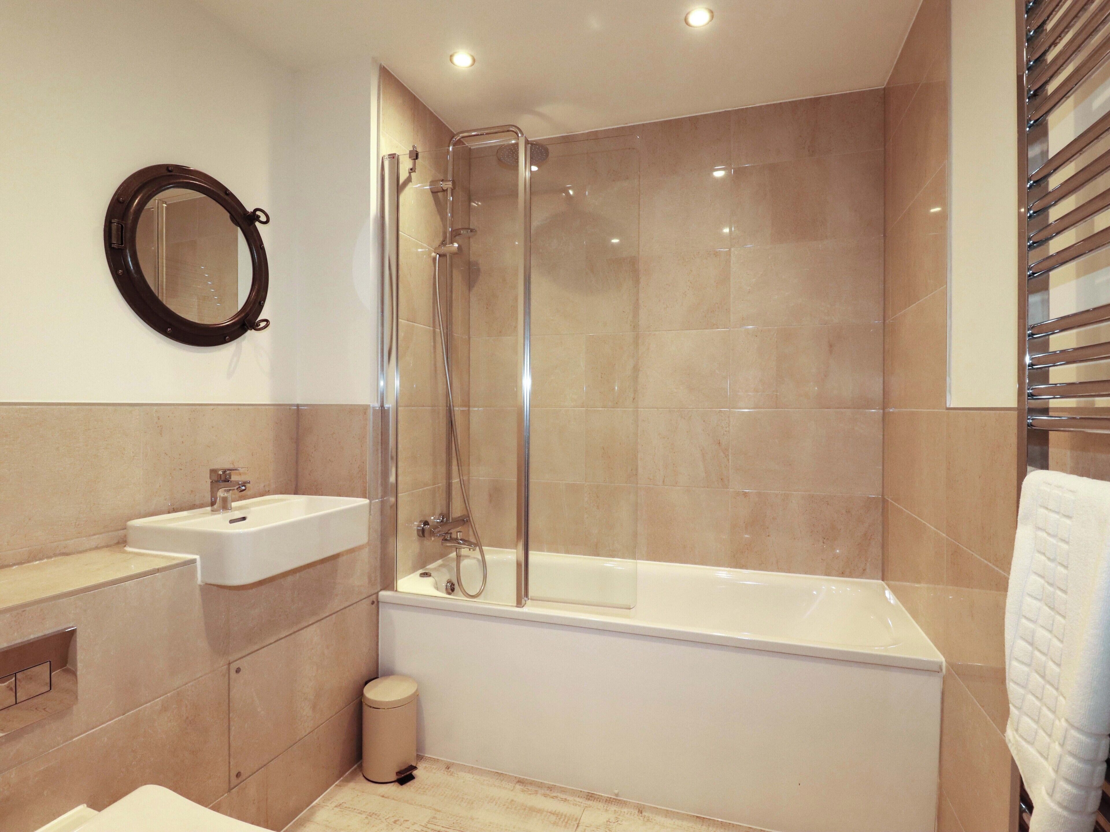 A modern bathroom with a glass-enclosed shower, a white bathtub, a sink, and a mirror.