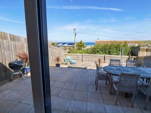 Eine Terrasse mit Tisch und Stühlen, einem Grill und Blick aufs Meer.
