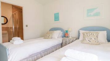 Habitación de hotel con dos camas, baño y una pequeña mesa con lámpara.