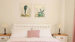 A bed with white and pink bedding, two pillows, two bedside tables with lamps, and two wall art pieces. - Serfaus (Perranporth)
