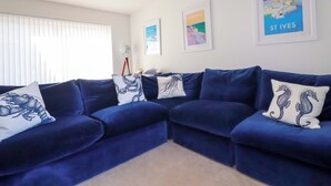 A living room with a blue sectional sofa, a floor lamp, and framed artwork on the walls. - Serfaus (Perranporth)
