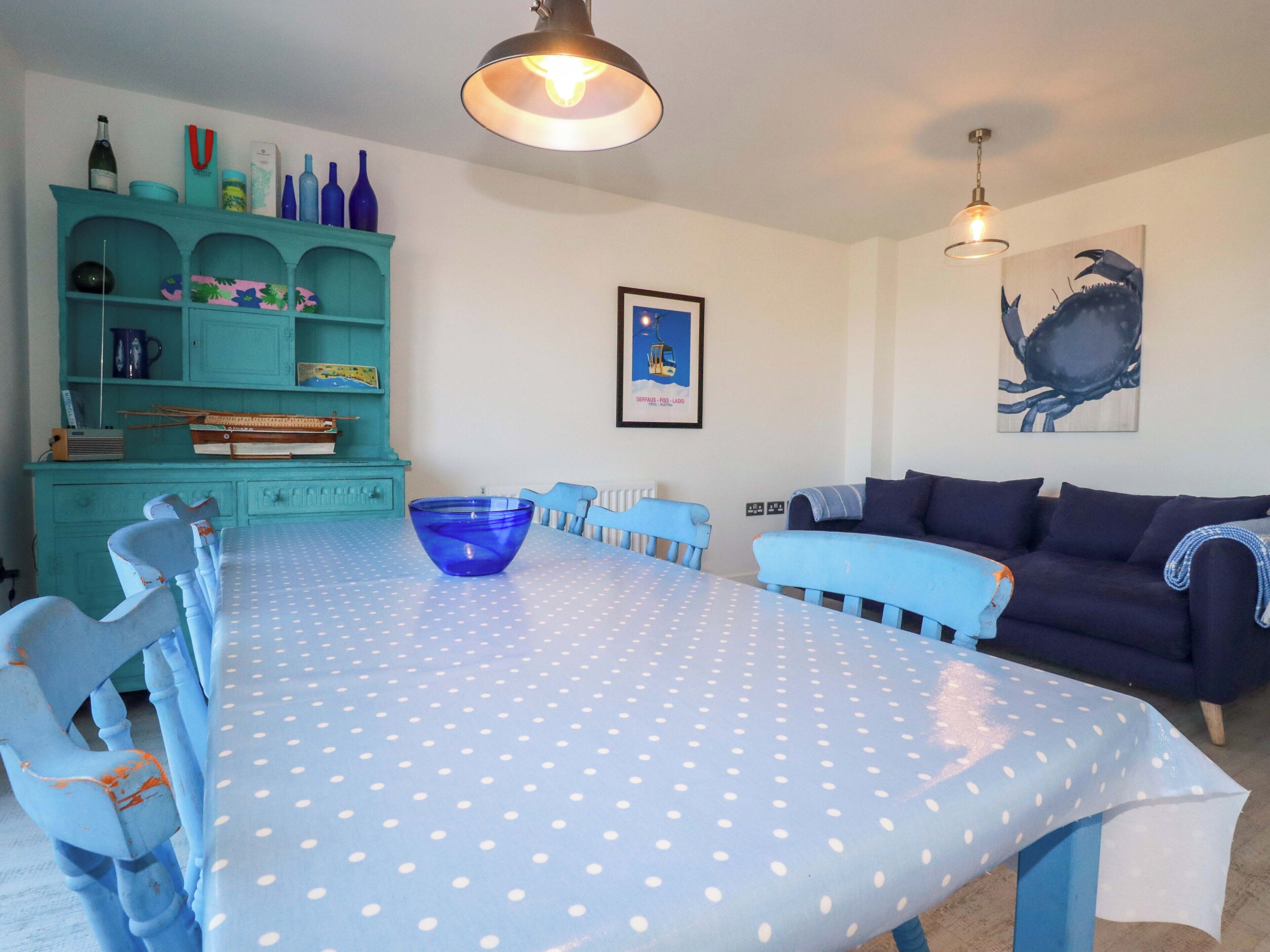 Een eetruimte met een blauwe tafel, teal stoelen en een teal kast met flessen.