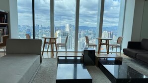 A modern living room with a sofa, two chairs, a coffee table, and a bookshelf. Large windows offer a city view. - kl city center klcc by dome (Kuala Lumpur)