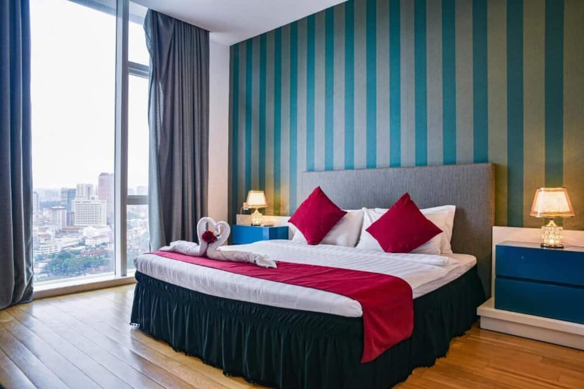 A hotel room with a large bed, two bedside tables, a view of the city, and striped wallpaper.