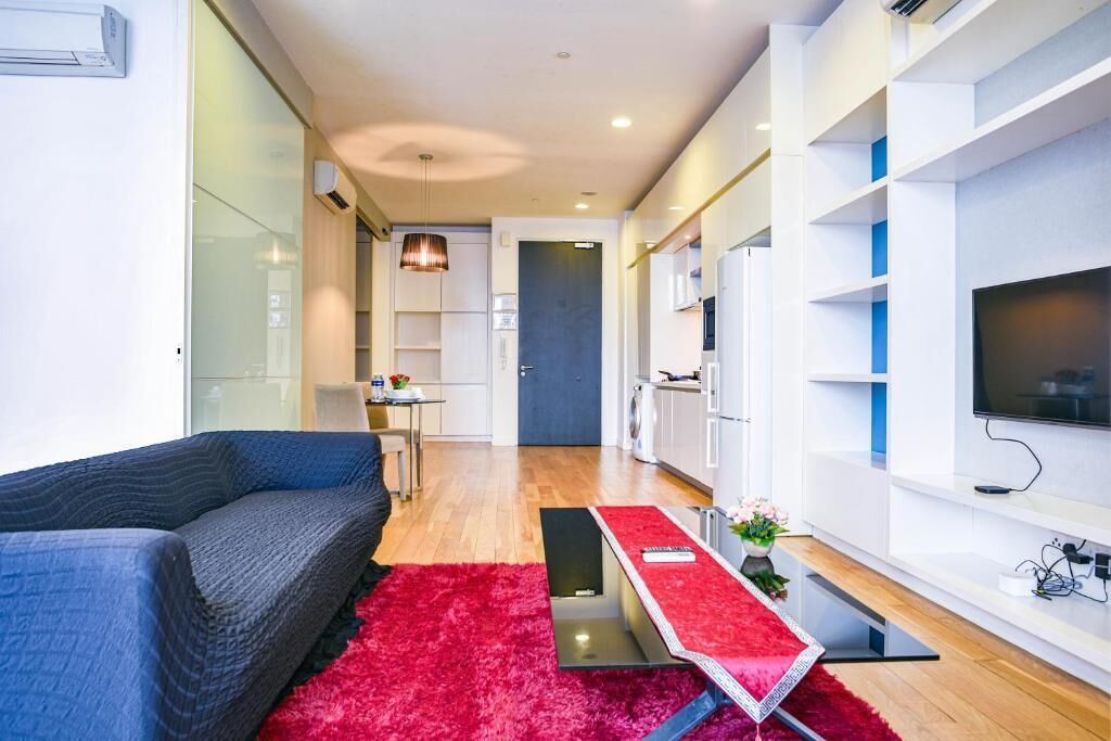 Een moderne woonkamer met een bank, een rood vloerkleed, een eettafel en een televisie aan een witte muur.