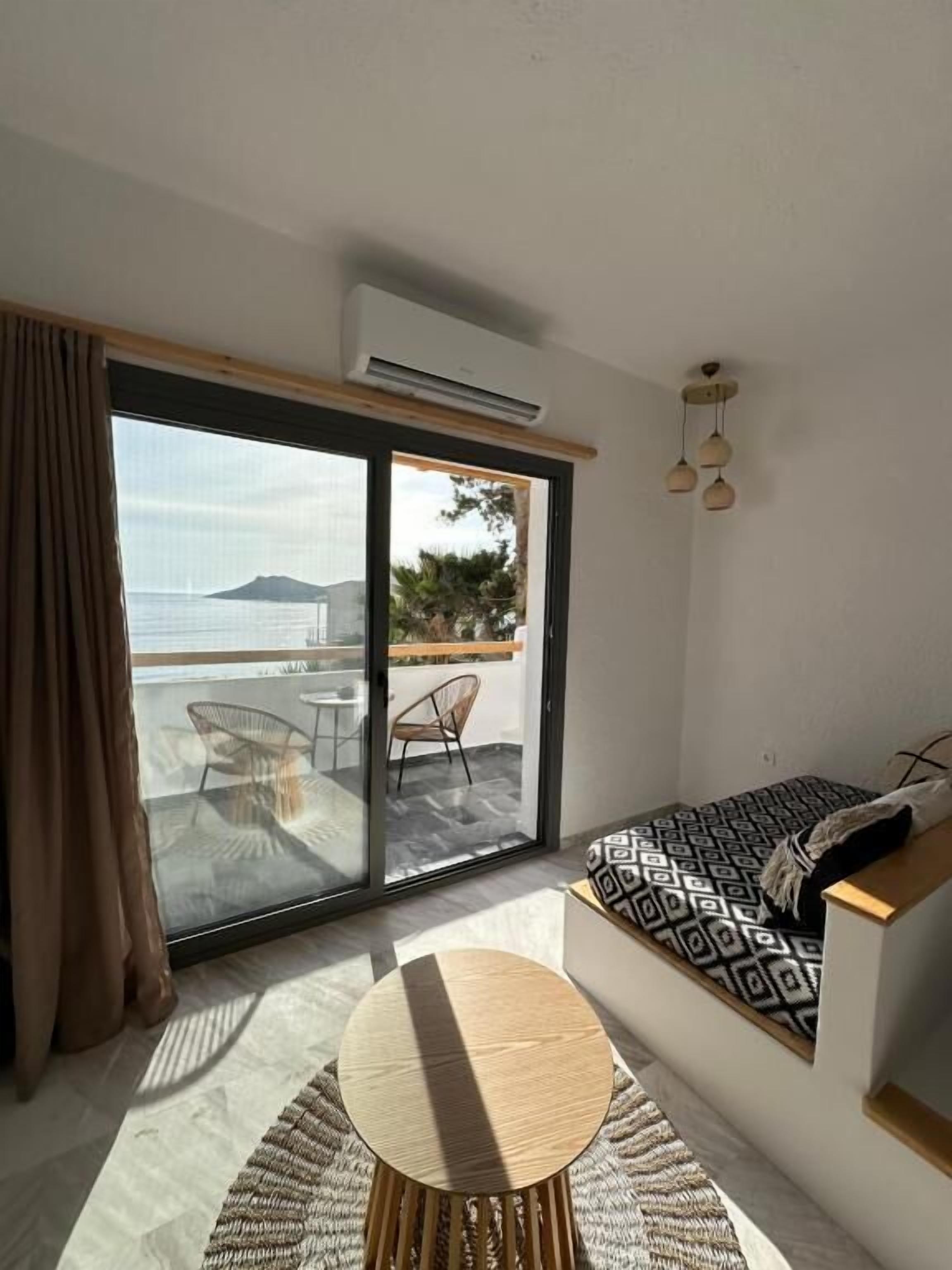 Una habitación moderna con una puerta de cristal corredera que da a un balcón, una mesa redonda de madera y un sofá estampado.