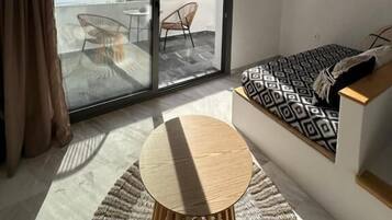 Una habitación moderna con una puerta de cristal corredera que da a un balcón, una mesa redonda de madera y un sofá estampado.