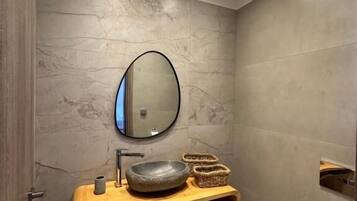 Un baño moderno con tocador de madera, espejo redondo y lavamanos grande.