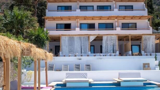 Un resort con piscina, edificio blanco y montañas al fondo.