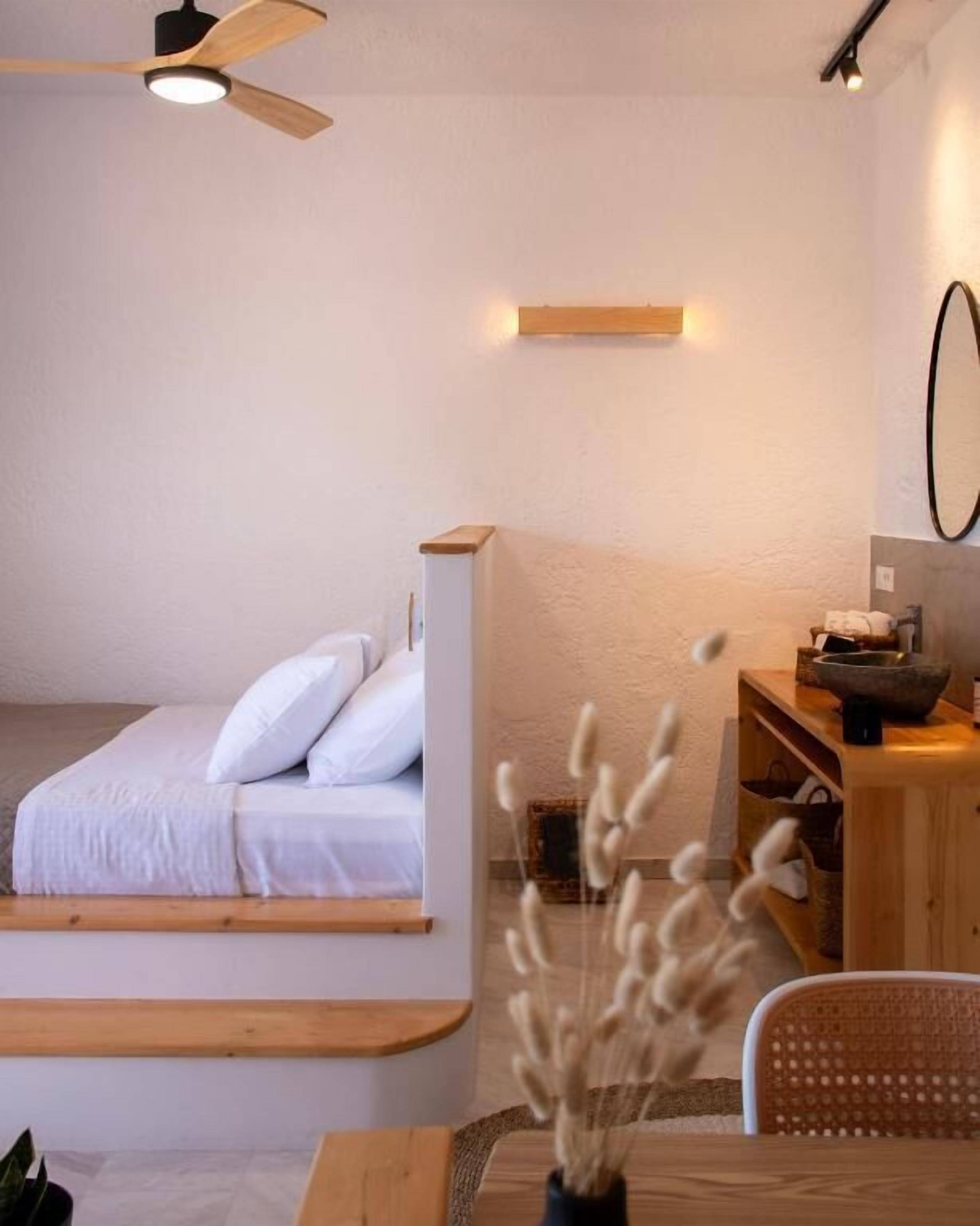 Un dormitorio con una cama, una mesita de noche de madera, una mesa con un florero y un ventilador de techo.