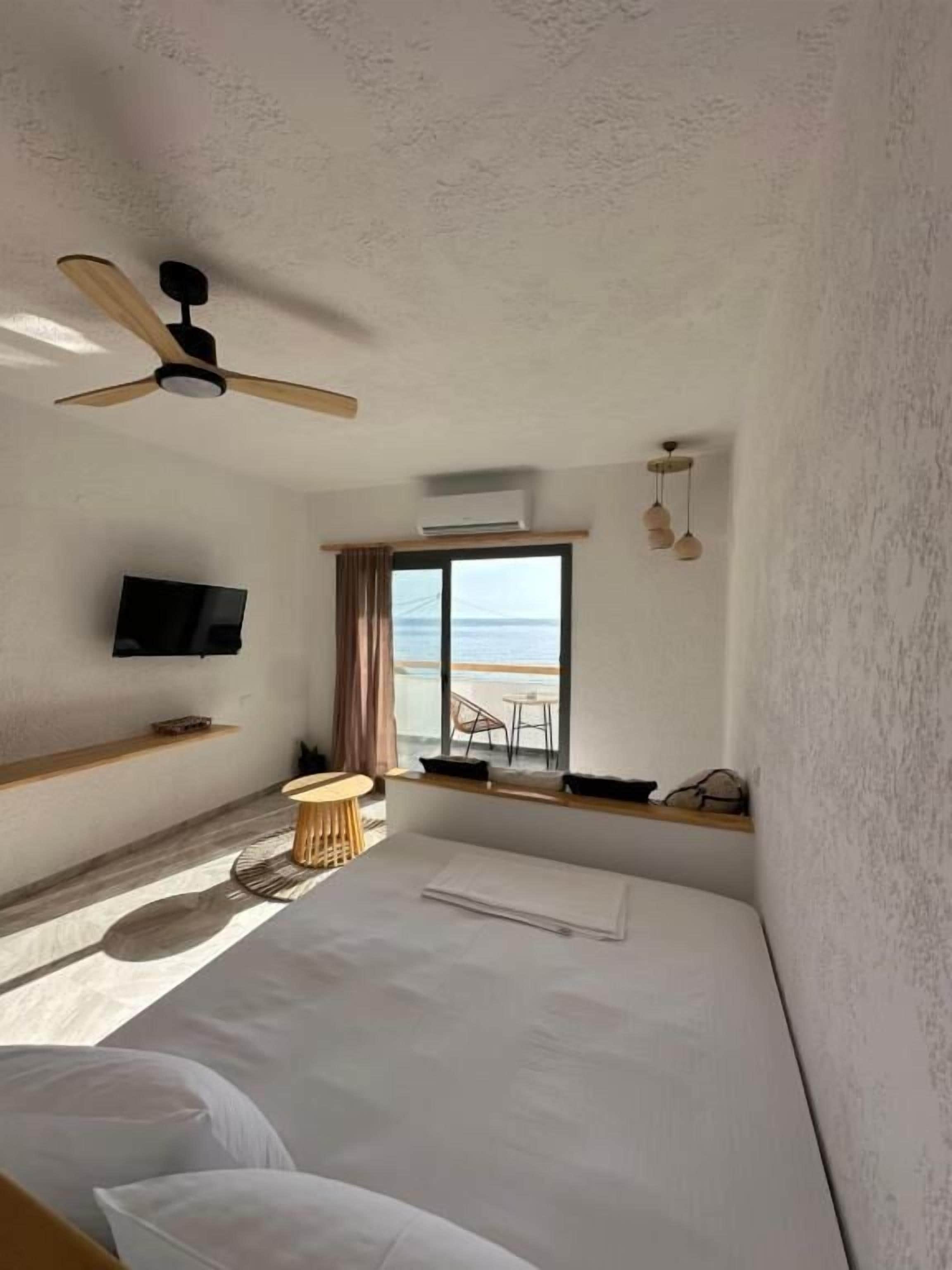Una habitación de hotel con cama, televisor, ventilador de techo, ventana con vistas y una mesita.