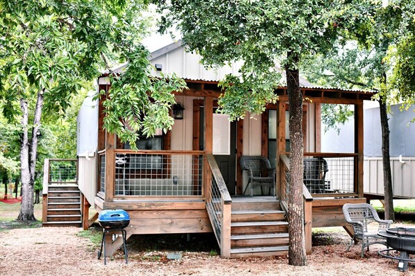Une cabane en bois avec une véranda, un barbecue et une chaise.
