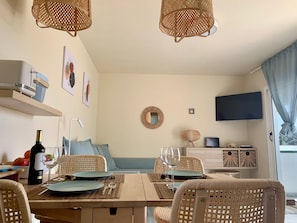 Een eetgedeelte met rieten stoelen, een houten tafel en een televisie aan de muur.