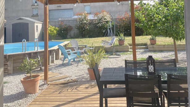 Een overdekt terras buiten met een zwembad, zitplaatsen en potplanten.