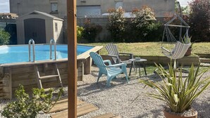 Een zwembadgedeelte met een pergola, lounge fauteuils en potplanten.