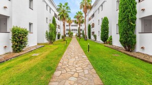 A courtyard with a stone pathway, palm trees, and neatly trimmed hedges. - Corsican Seaview Coastal Stay for 6 (San-Nicolao)