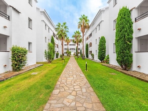 A courtyard with a stone pathway, palm trees, and neatly trimmed hedges. - Corsican Seaview Coastal Stay for 6 (San-Nicolao)