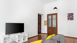 A modern living room with a flat-screen TV on a white stand, a wooden door, and a yellow cushion on a grey sofa. - Billy's House – Spacious comfort in the heart of Cagliari 🌿✨ (Cagliari)