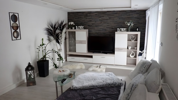 Un salón moderno con un televisor de pantalla plana, armarios blancos, una mesa de centro de vidrio y plantas decorativas.