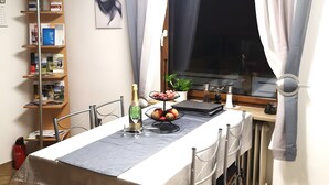 Una zona de menjador amb una taula posta per a dues persones, una estanteria, una finestra amb cortines i un radiador.