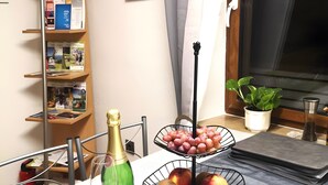 Habitació amb taula que mostra una ampolla de xampany, una cistella de fruita i una estanteria plena de llibres i revistes.