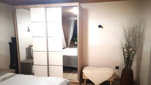 Un dormitori amb un llit, una tauleta de nit, una cadira, un armari i un vas amb flors seques.