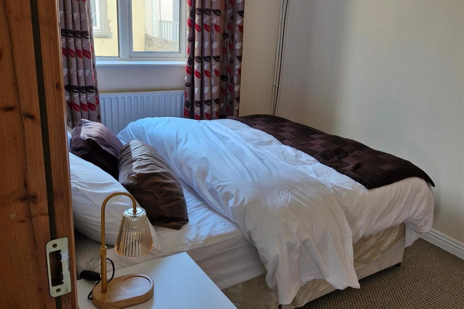 A single bed with white bedding, a brown throw blanket, and a bedside lamp.