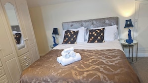 Una habitación de hotel con una cama, almohadas, una mesita de noche, una lámpara y un espejo.