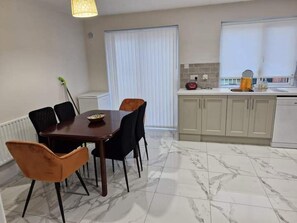 Uma área de refeições com mesa e cadeiras, uma cozinha com armários e pia, e uma janela com cortinas.