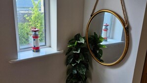 Una ventana con un modelo de faro rojo y blanco, un espejo con marco dorado y una planta en maceta.