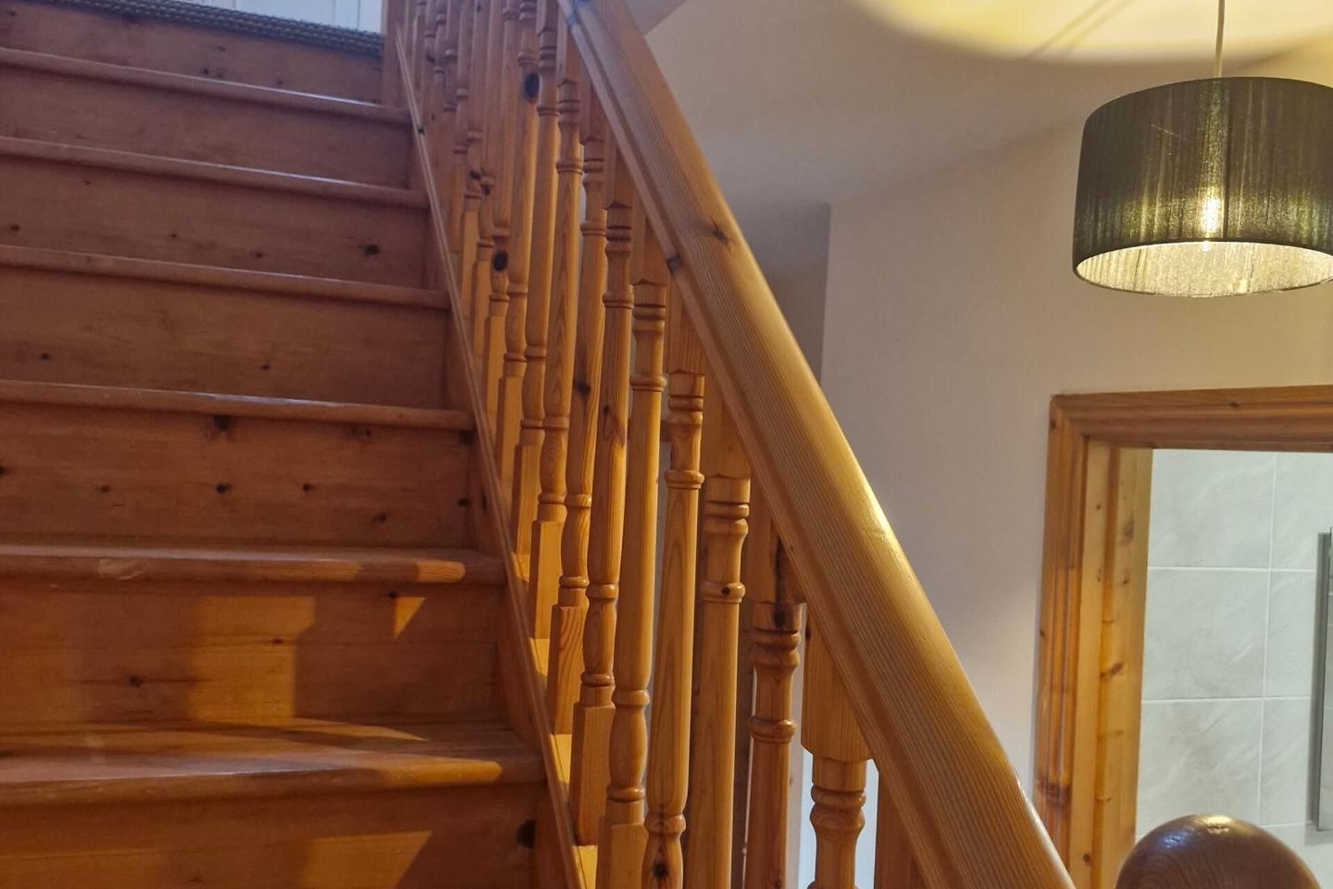 A wooden staircase with a handrail, a ceiling light fixture, and a door in the background.